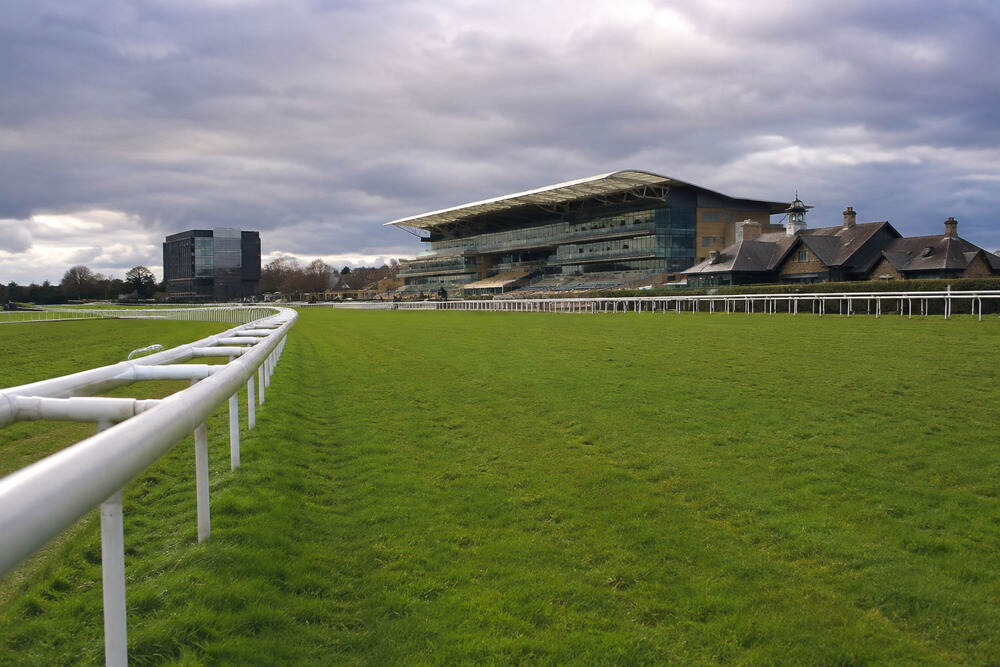 View of Doncaster Racecourse with its turf track, white rails and grandstands under a cloudy sky.